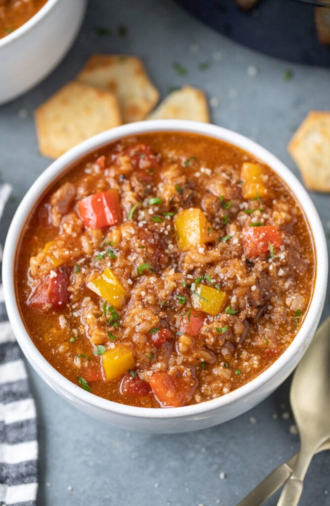A bowl of stuffed bell pepper soup with crackers on the side on a grey background