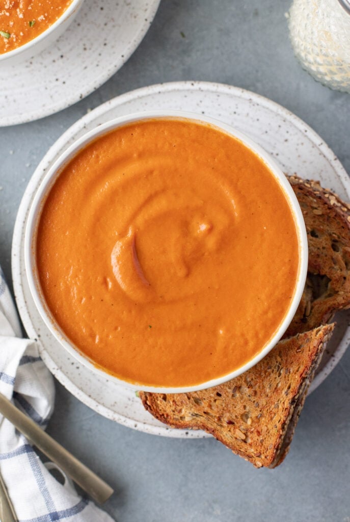 An overhead shot of tomato basil soup with grilled cheese on the side
