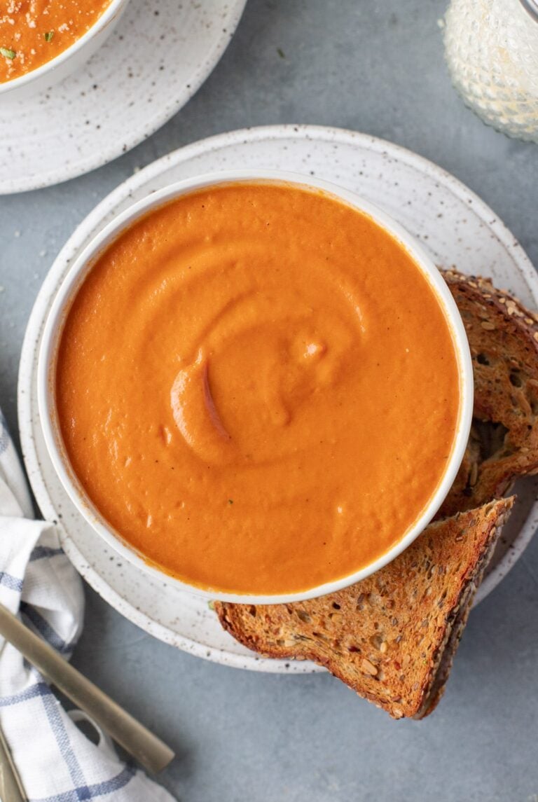 An overhead shot of tomato basil soup with grilled cheese on the side