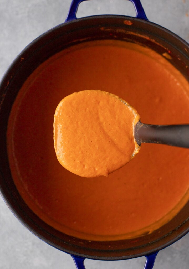 A stock pot of tomato basil soup with a ladle getting a big scoop out of it