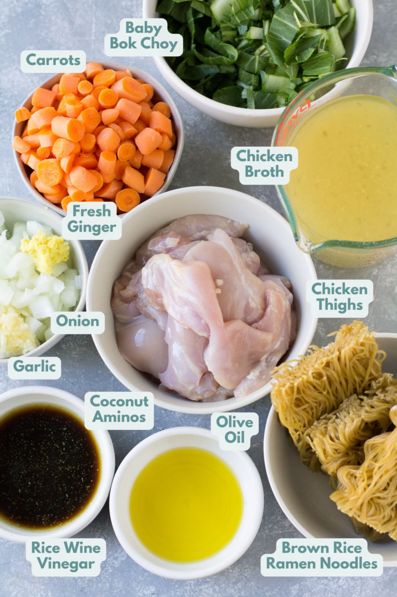 Ingredients for Asian Chicken Soup in small white bowls: onions, carrots, ginger, bok choy, broth, chicken thighs, ramen, olive oil, coconut aminos and rice wine vinegar.