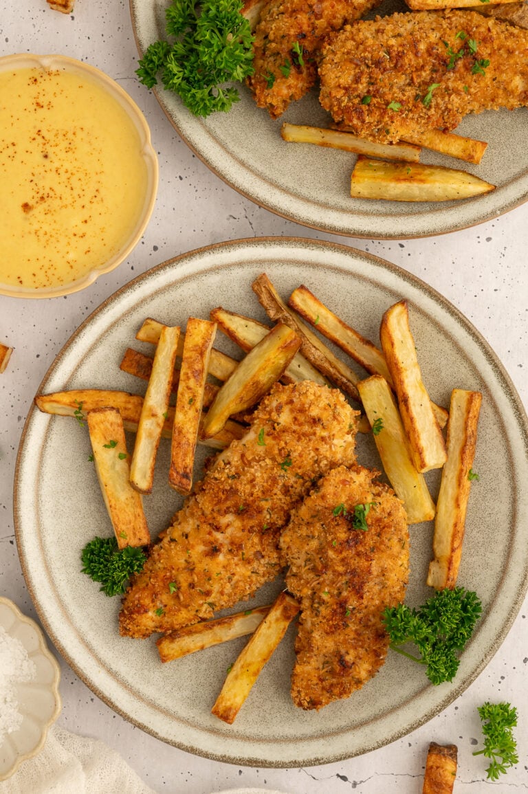 Baked chicken tenders + fries on a plate with a another plate of food and a bowl of honey mustard off to the side.