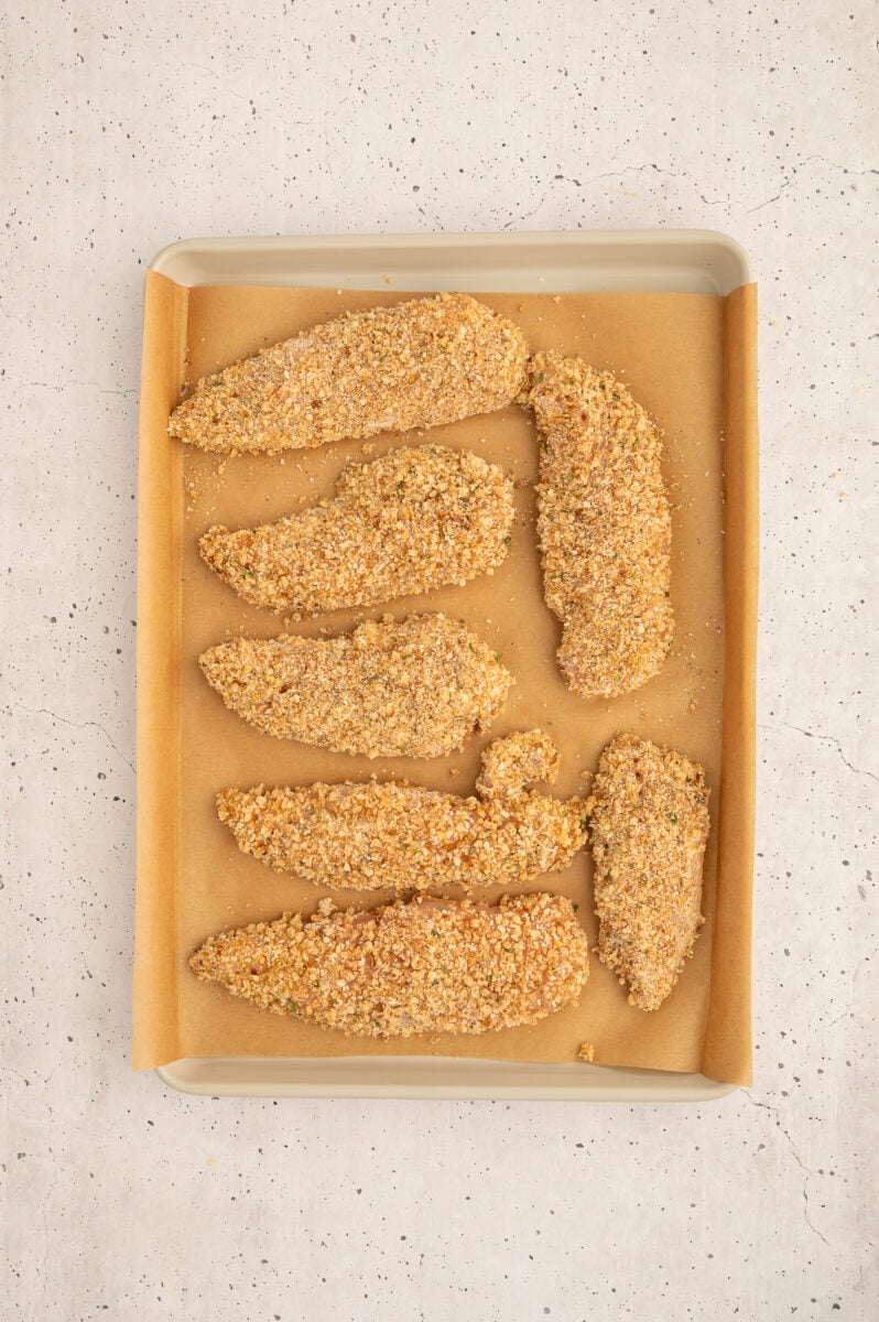 Raw healthy chicken tenders on a parchment lined baking sheet.