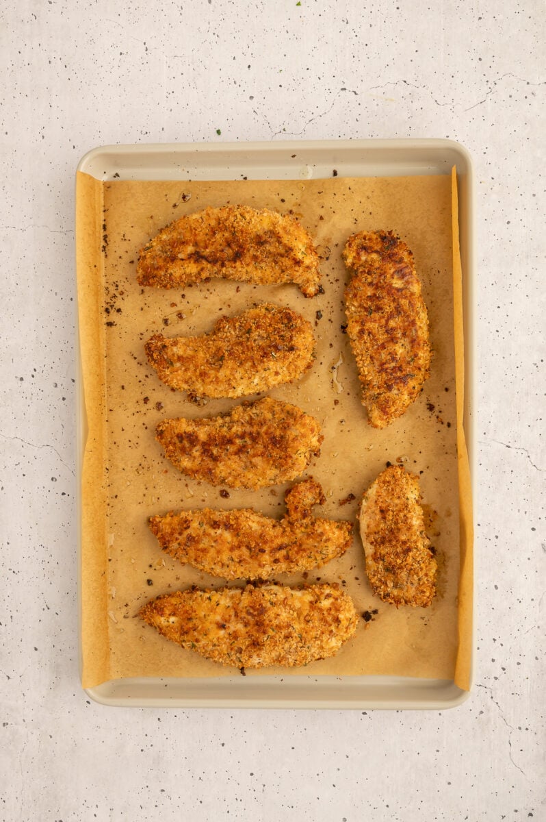 Healthy chicken tenders on a parchment lined baking sheet.