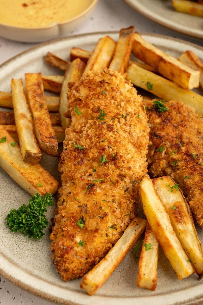 A close up of baked chicken tenders on a bed of fries on a plate.