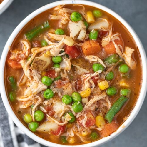 an overhead shot of chicken vegetable soup on a grey background