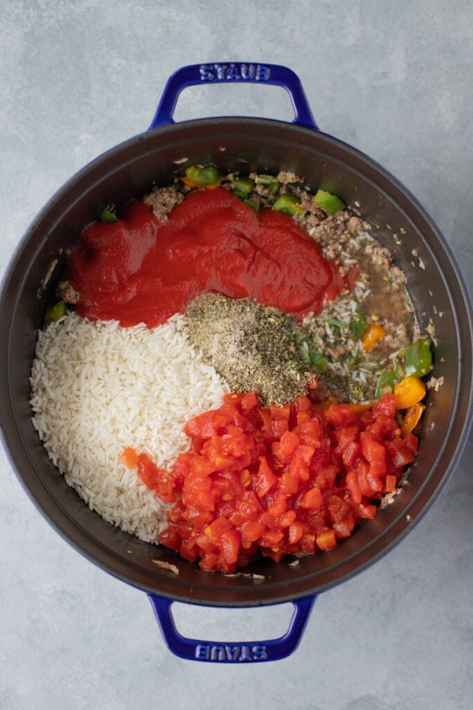 a dutch oven with garlic, onion, peppers, beef, tomato sauce, tomatoes, salt, pepper, oregano, basil, rice and beef broth unmixed for stuffed bell pepper casserole