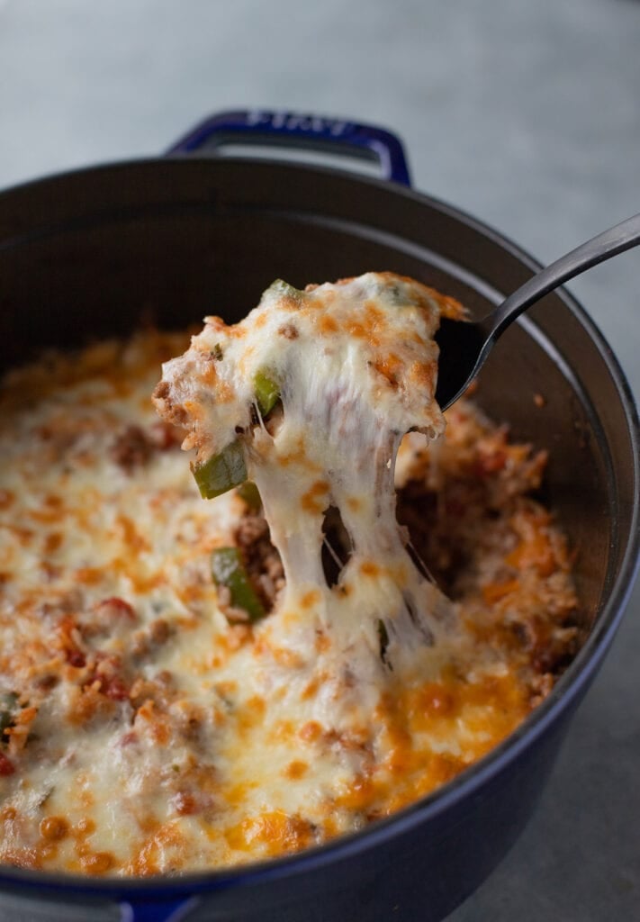 a dutch oven of stuffed pepper casserole with a spoonful being taken out with a cheese pull