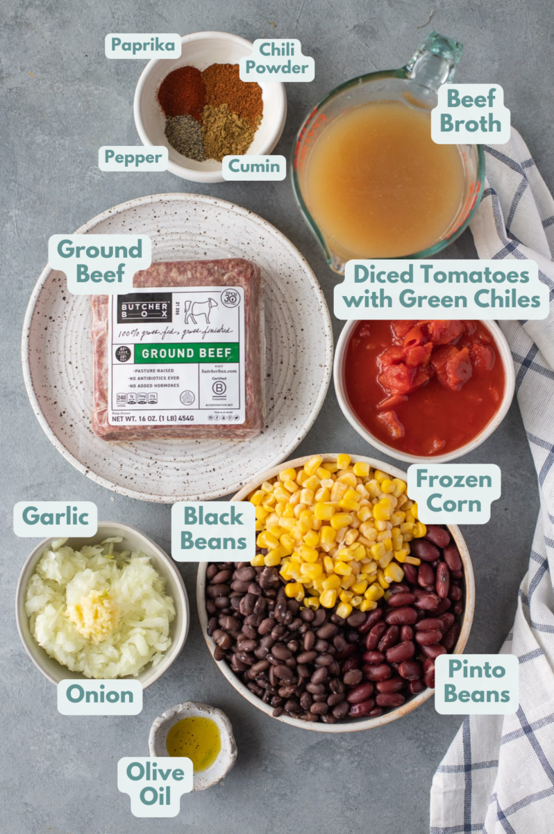 Ingredients for taco soup in small white bowls: olive oil, ground beef, onion, garlic, diced tomatoes with green chiles, beef broth, paprika, pepper, chili powder, cumin, black beans, pinto beans, frozen corn
