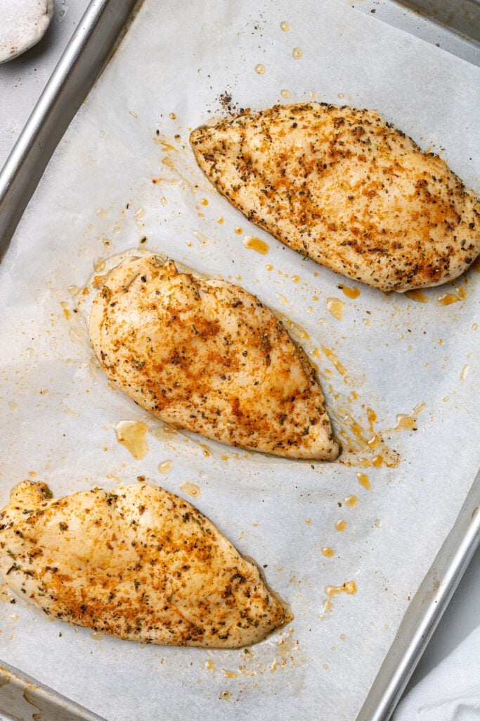 Boneless chicken breasts fully cooked on a parchment lined sheet pan