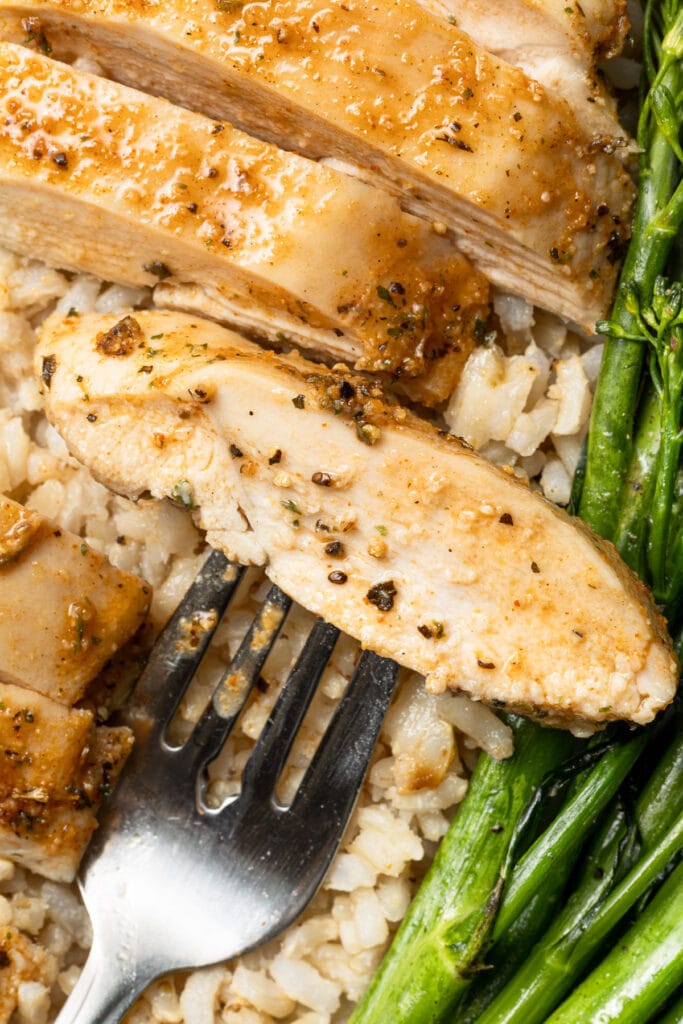 a slice of boneless chicken breast on a fork with a background of rice and broccolini
