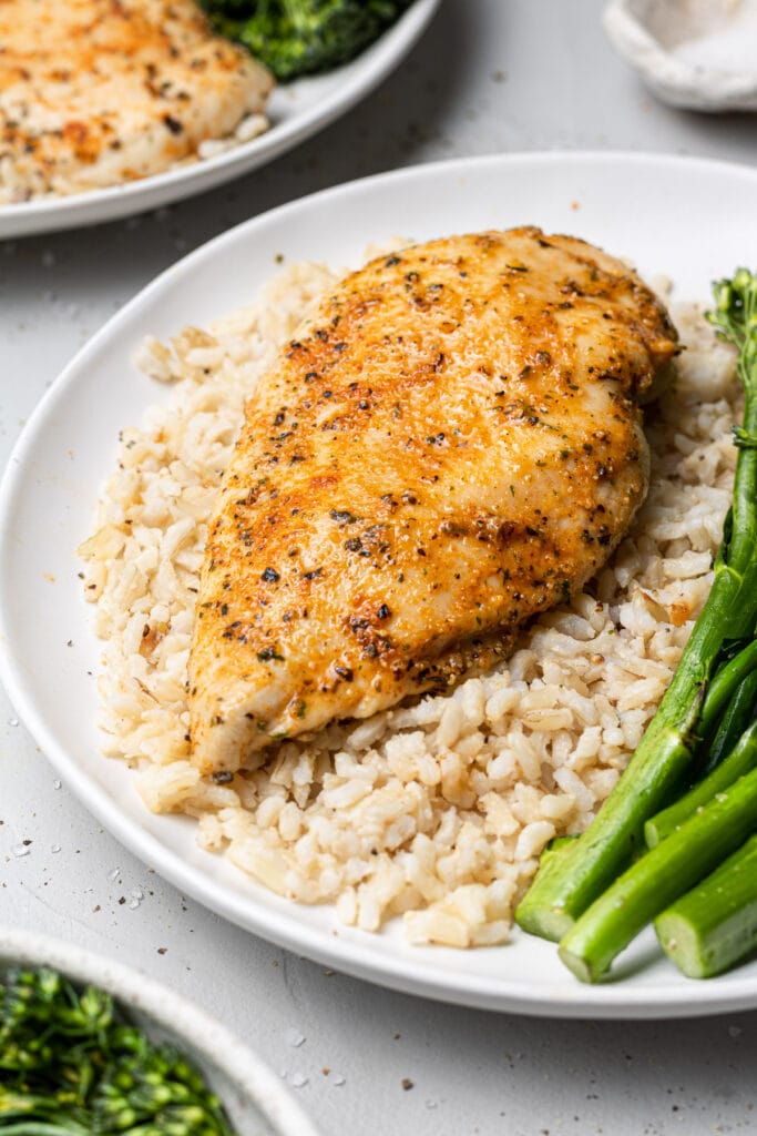 Baked boneless chicken breast on a white plate with rice and broccolini