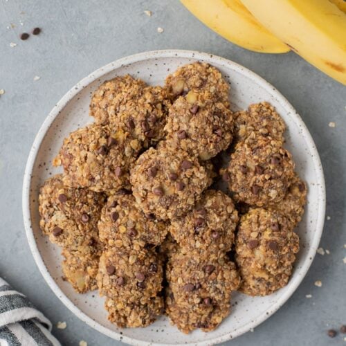 An overhead shot of healthy banana breakfast cookies on a white plate with a grey background