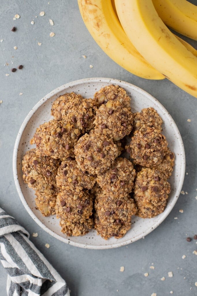 An overhead shot of healthy banana breakfast cookies on a white plate with a grey background