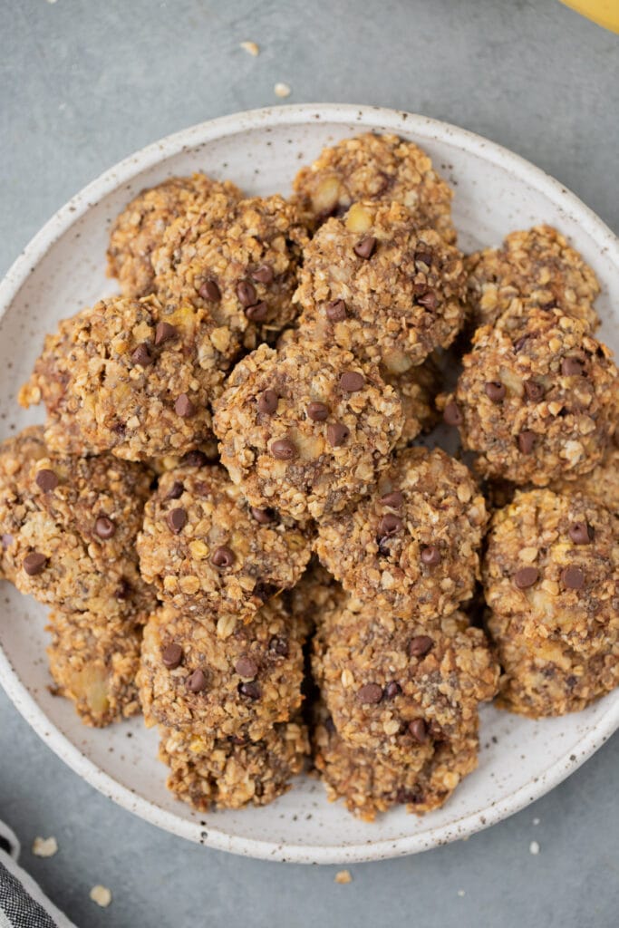 An overhead shot of healthy banana breakfast cookies on a white plate with a grey background