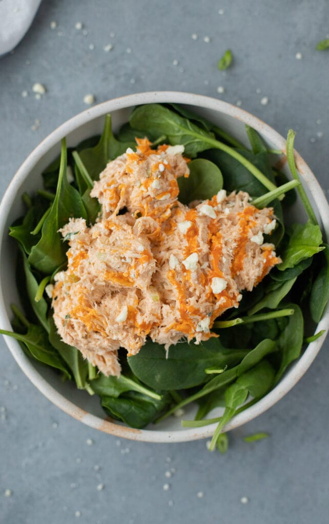 buffalo chicken salad on top of spinach in a white bowl on a grey background