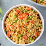 An overhead shot of fried cauliflower rice in a white bowl on a grey background