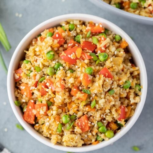 An overhead shot of fried cauliflower rice in a white bowl on a grey background