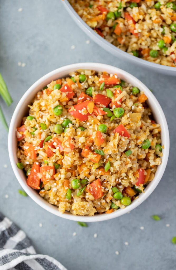 An overhead shot of fried cauliflower rice in a white bowl on a grey background