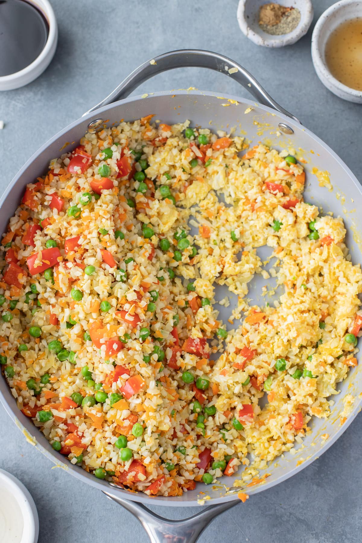 Sautéd veggies in a pan for cauliflower fried rice pushed to the side with cooked scrambled eggs on the side