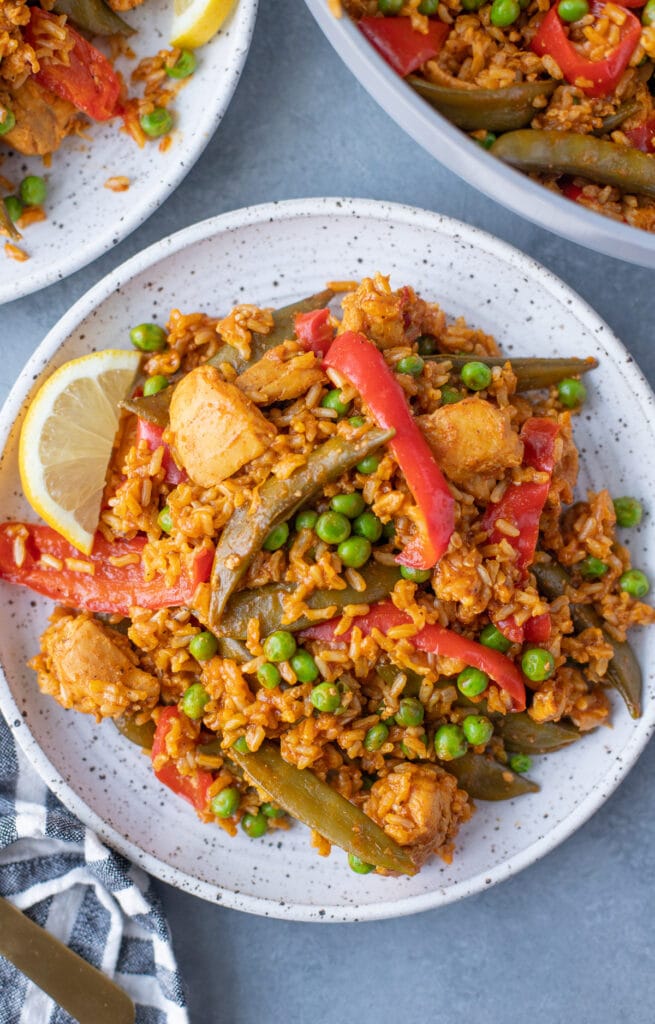 An overhead shot of chicken paella on a white plate on a grey background