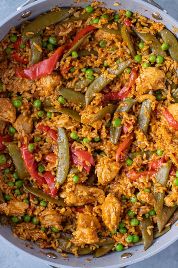 An overhead shot of a pan of chicken paella on a grey background