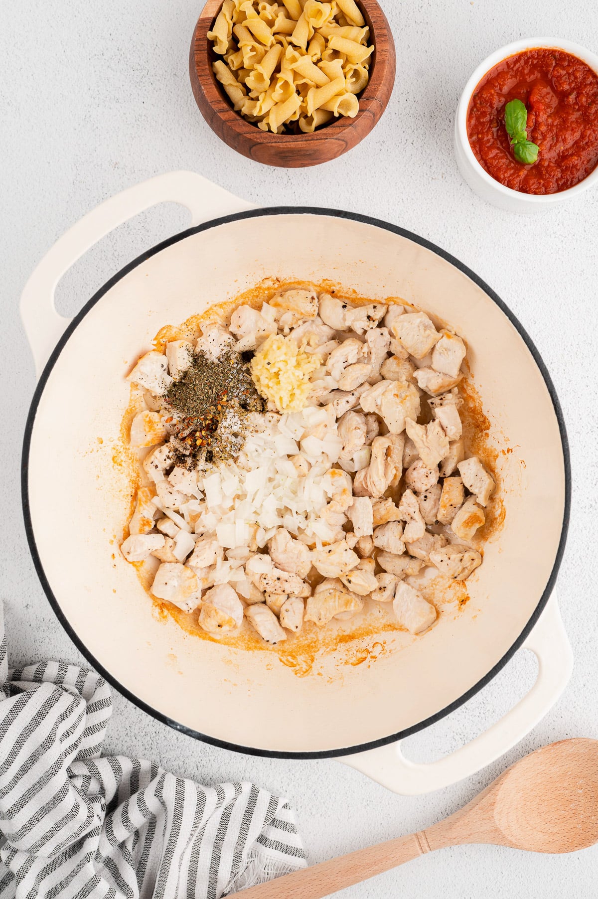 An overhead shot of a dutch oven with browned chicken and herbs for chicken parm pasta