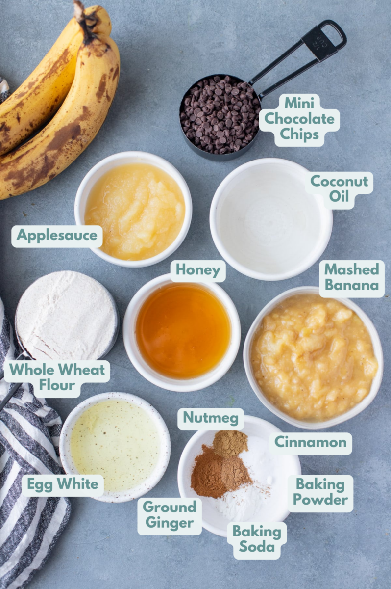 Healthy Banana Bread ingredients in white bowls: Bananas, flour, egg, coconut oil, honey, applesauce, chocolate chips and spices