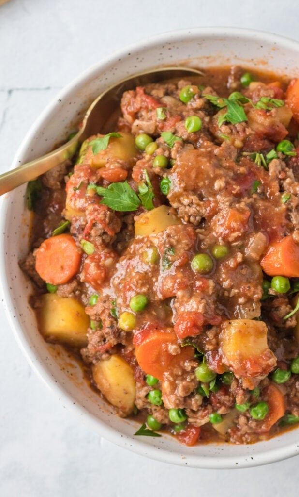 A close up of healthy hamburger stew on a white marble background with a gold spoon taking a bite out of it