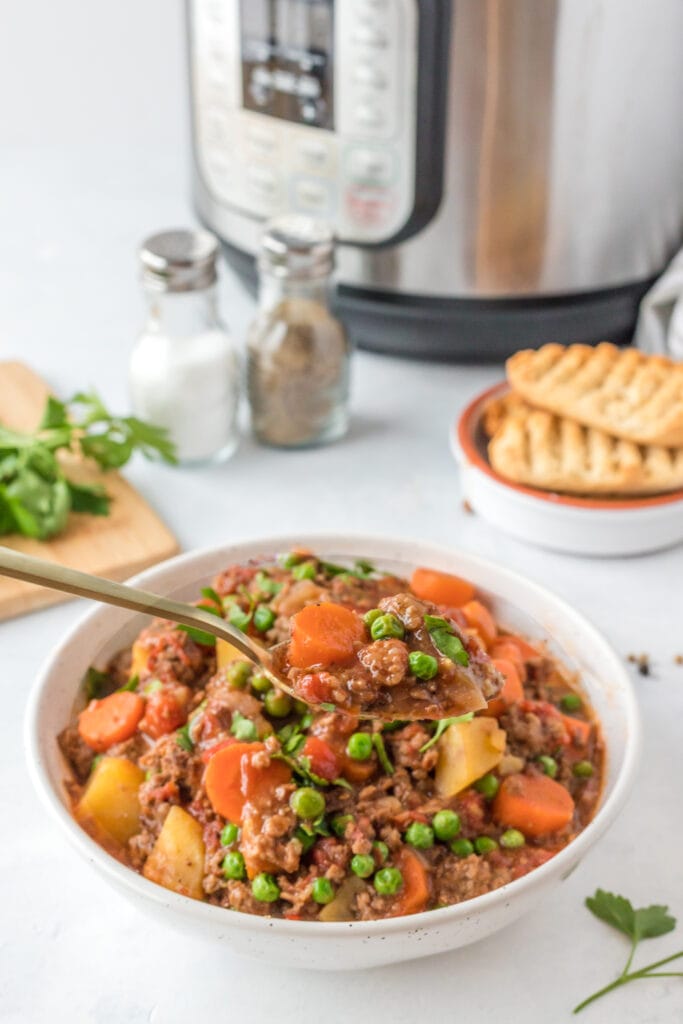 A spoon taking a bite out of ground beef stew with an instant pot in the background