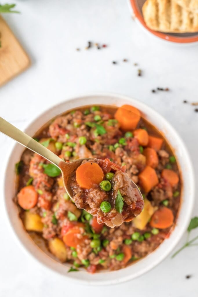 a spoon taking a bite out of hamburger stew with potatoes