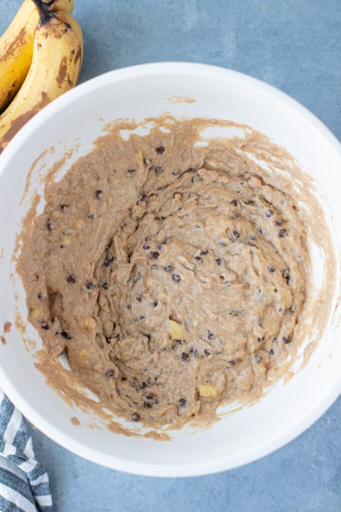 Ingredients for healthy banana bread in a white bowl mixed together with bananas on the side