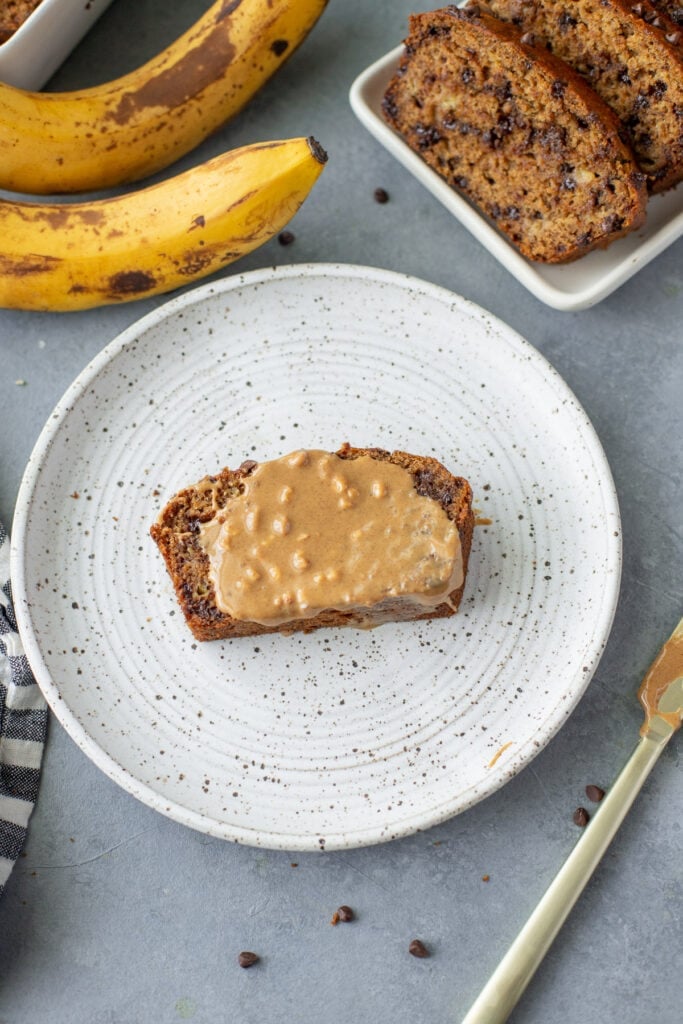 Healthy Banana Bread with peanut butter on it and a plate of bread and bananas on the side