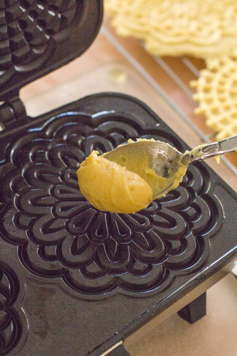 A spoon dropping pizzelle dough into a pizzelle press.