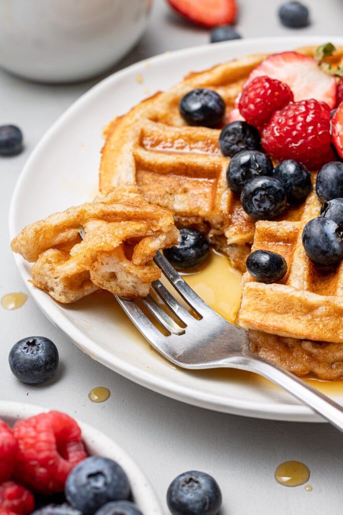 healthy protein waffles with strawberries and blueberries on top with a fork taking a bite out of it