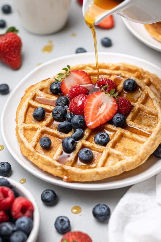 healthy protein waffles with strawberries and blueberries on top with syrup being poured on top