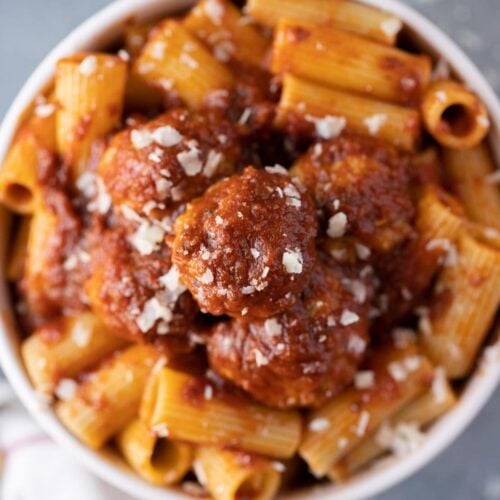 A white bowl filled with healthy turkey meatballs covered in sauce and on top of noodles
