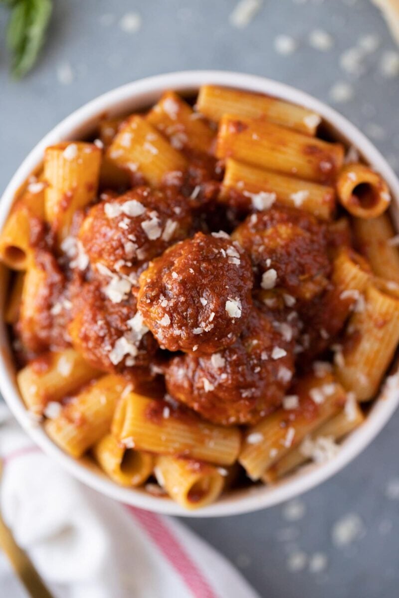 A white bowl filled with healthy turkey meatballs covered in sauce and on top of noodles