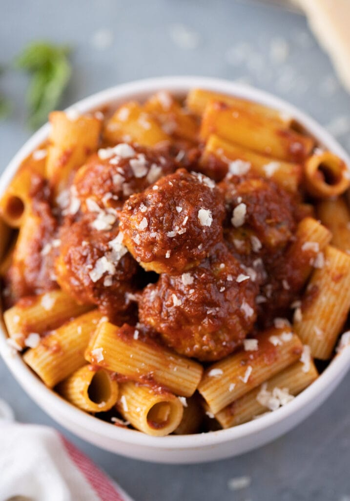a white bowl filled with Italian turkey meatballs and pasta on a grey background