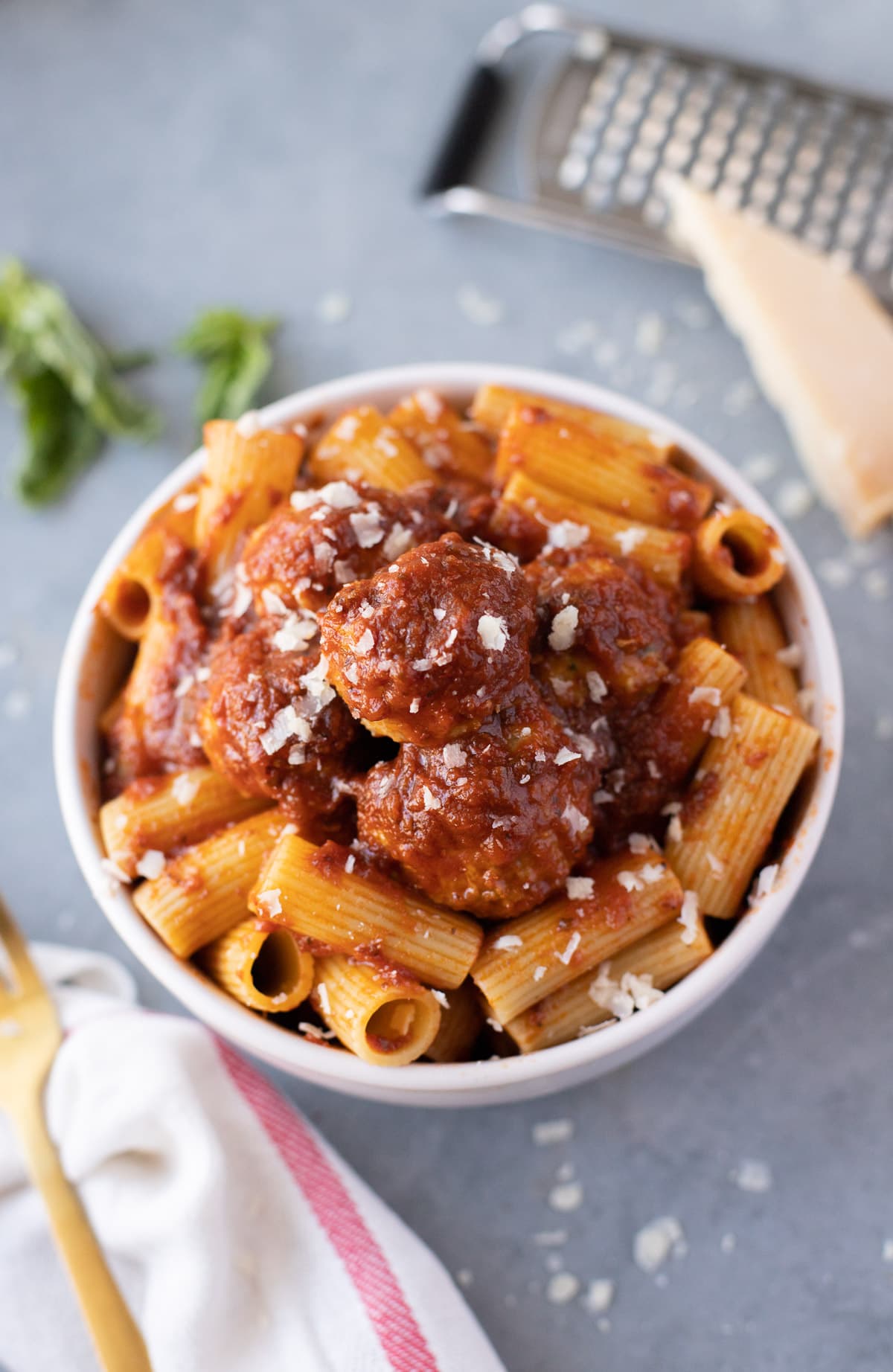 Italian turkey meatballs with red sauce and ziti in a white bowl on a grey background. Fresh Parmesan cheese is grated over the meal.