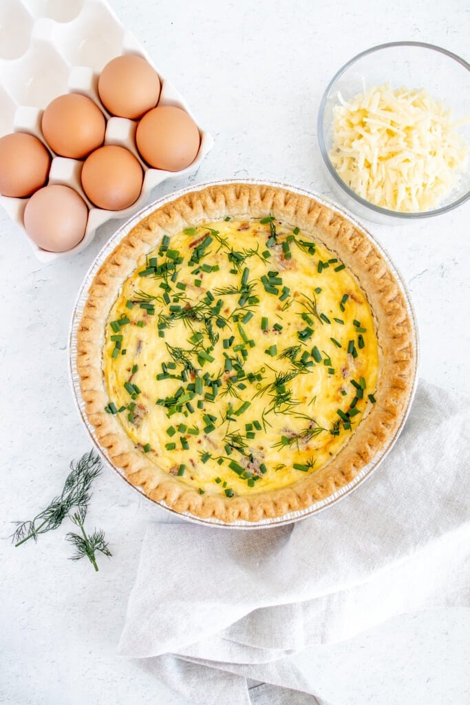 bacon and cheese quiche with fresh herbs on top with eggs and cheese on the side