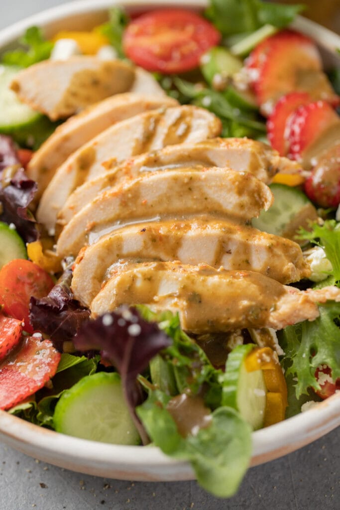 creamy balsamic dressing on a salad with sliced grilled chicken, cucumbers, tomatoes and strawberries on top