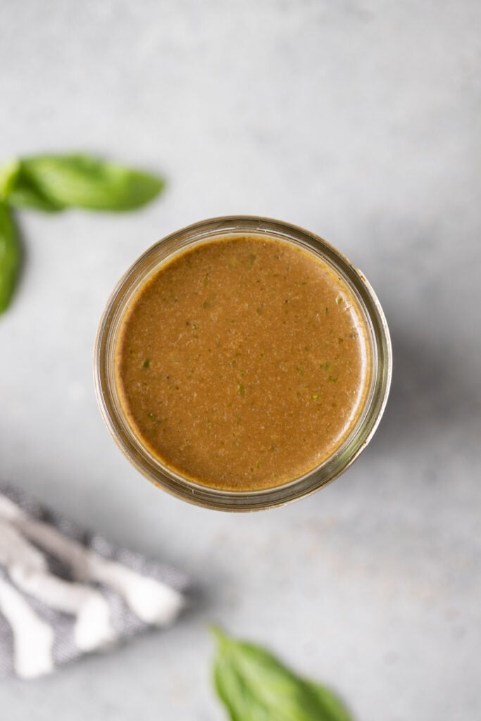 an overhead shot of creamy balsamic dressing in a mason jar on a grey background with basil on the side