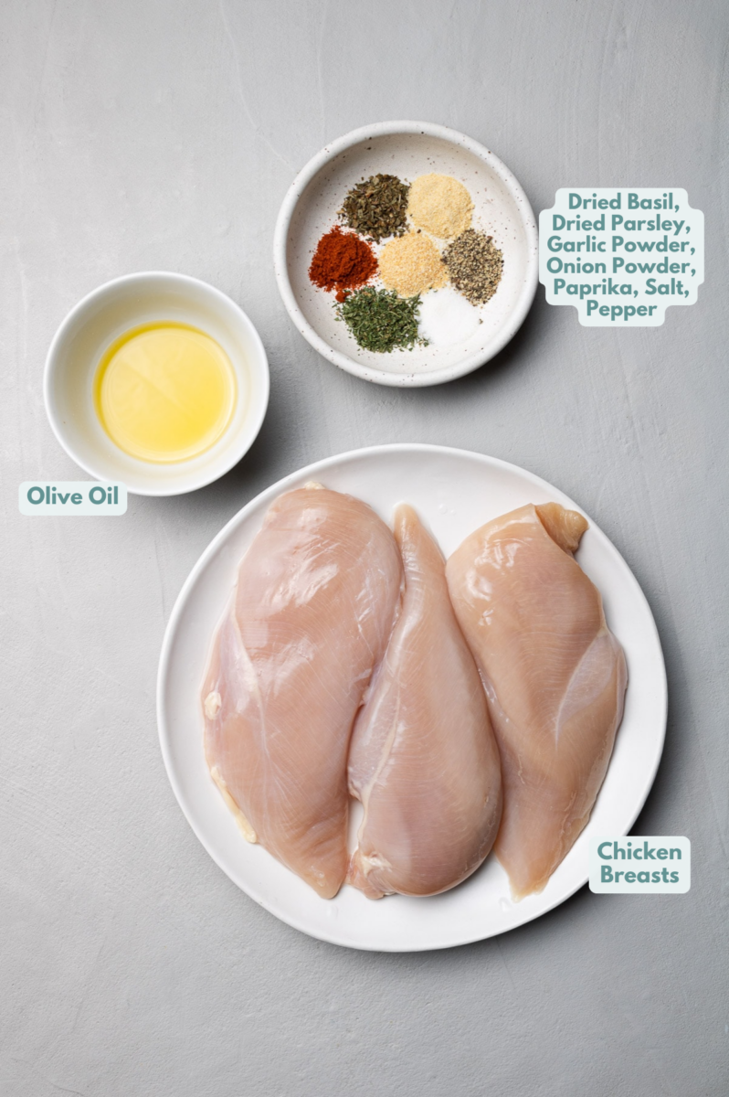 Ingredients for baked boneless chicken breast in white bowls: boneless, skinless chicken breasts, olive oil, paprika, dried basil, dried parsley, garlic powder, onion powder, pepper, salt