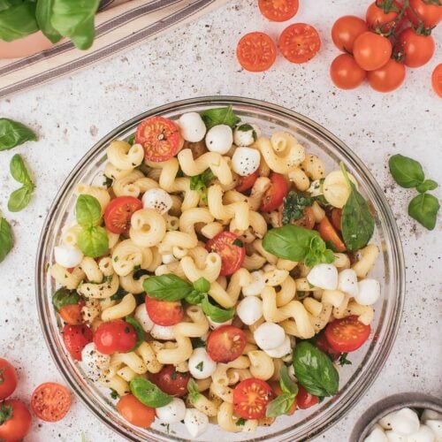 A large bowl of caprese pasta salad with mozzarella pearls and tomatoes on the side