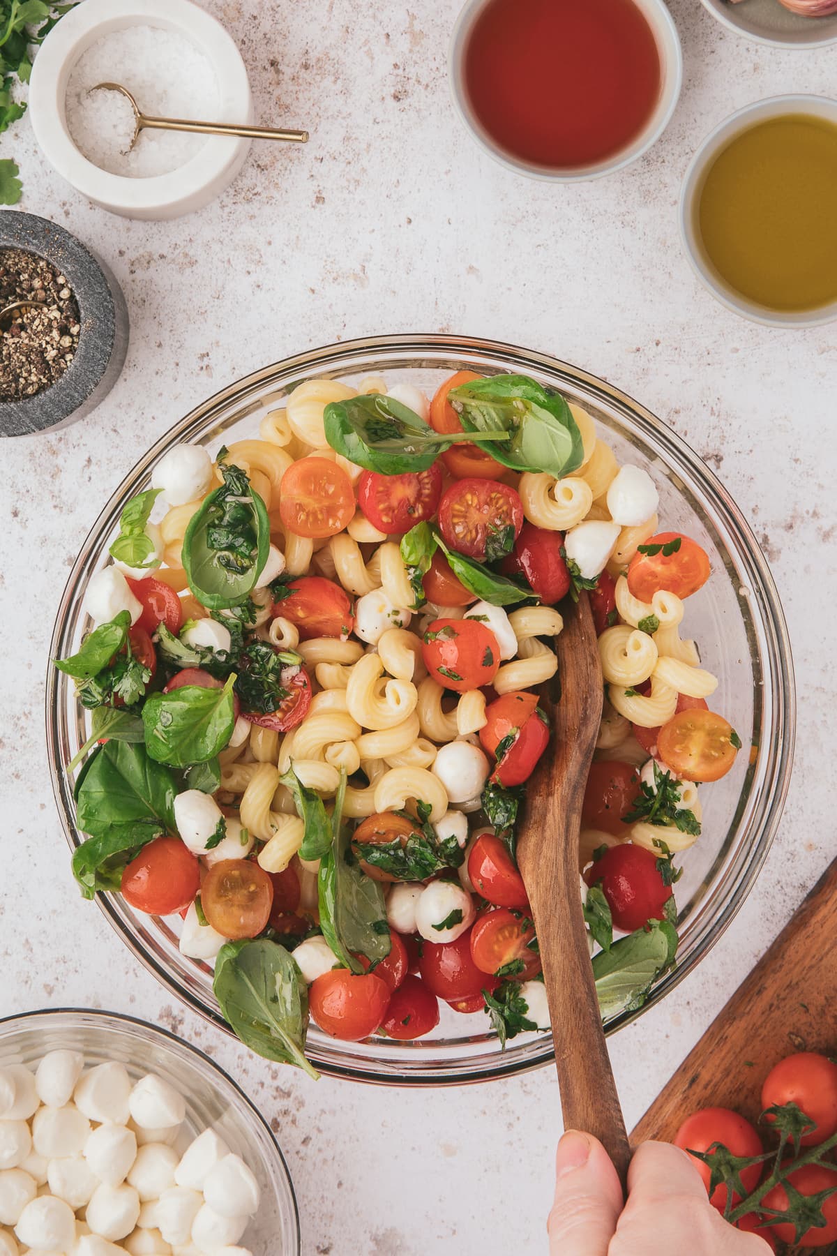 caprese pasta salad being mixed in a clear bowl on a white background