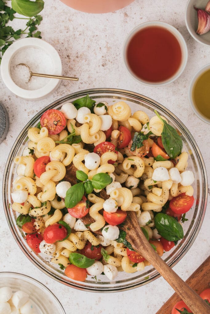 A large bowl of caprese pasta salad being mixed with a wooden spoon