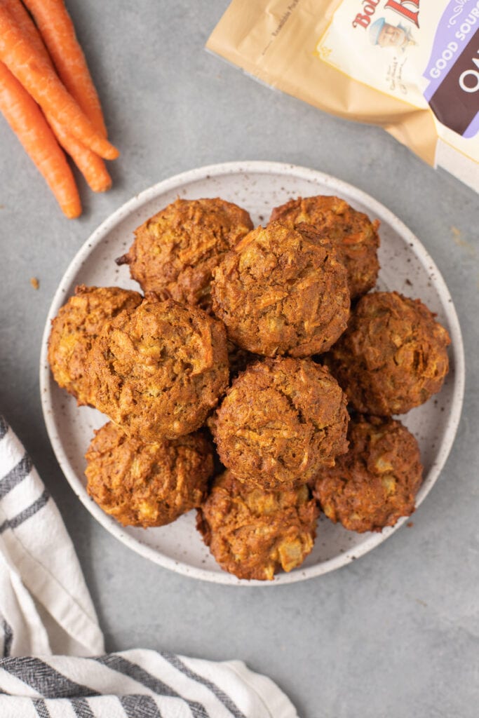 Healthy carrot muffins on a white plate with a grey background and carrots on the side