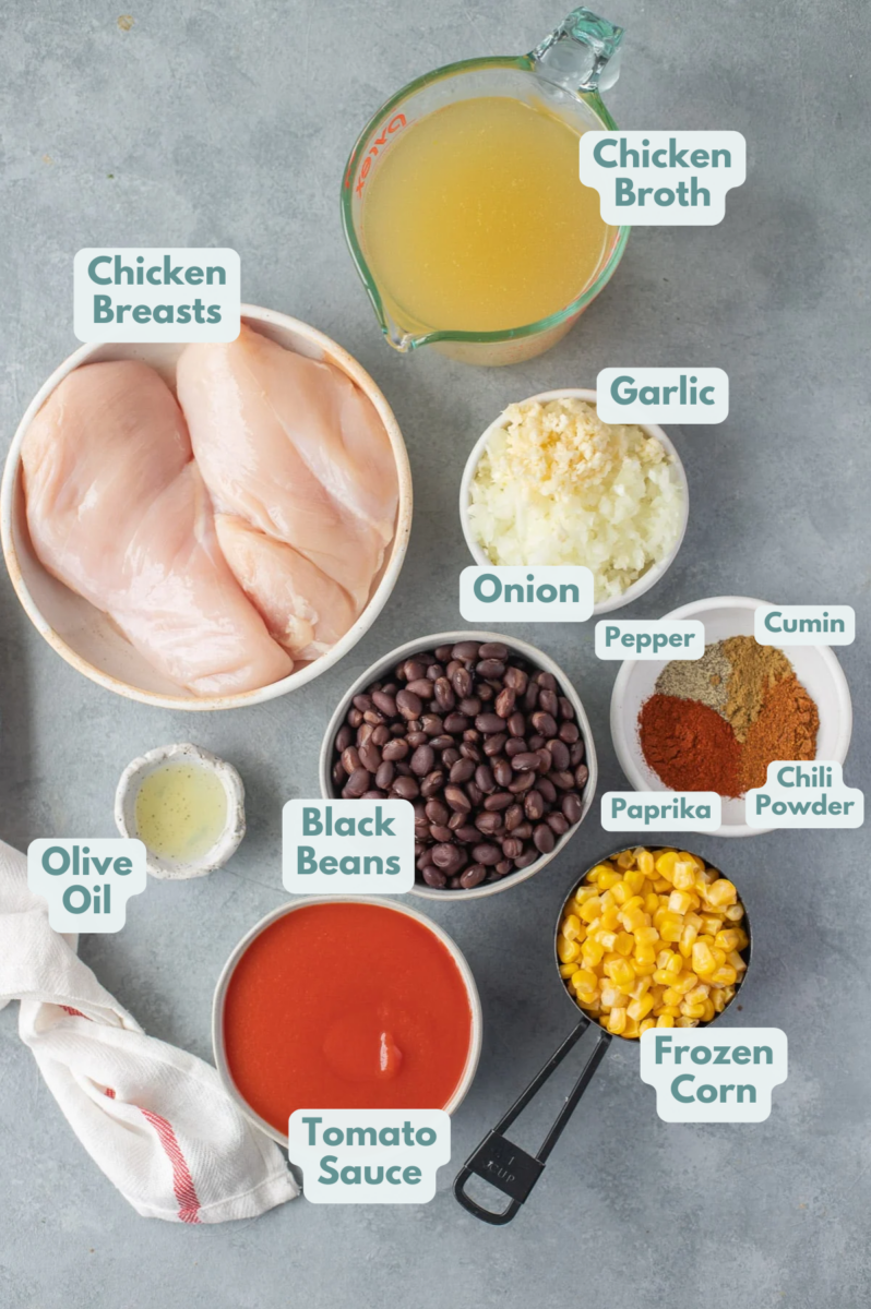 Ingredients for chicken taco soup in white bowls: olive oil, onion, garlic, chicken breasts, tomato sauce, chicken broth, paprika, pepper, chili powder, cumin, black beans, frozen corn