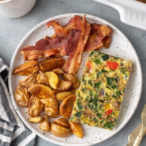 an overhead shot of healthy breakfast casserole on a white plate with bacon and crispy potatoes
